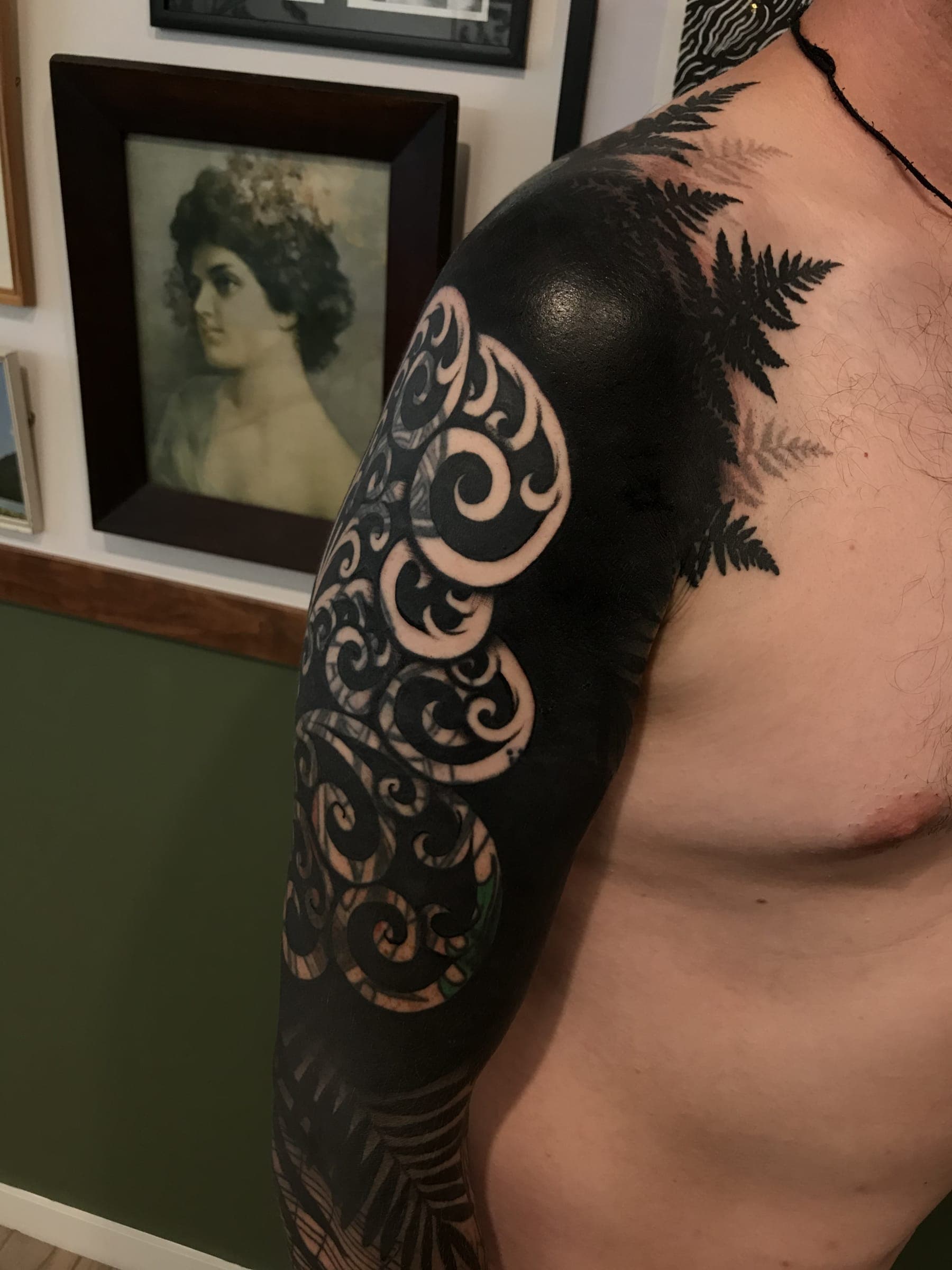 Solid black tattoo with koru spirals in negative space and silhouetted fern fronds reaching