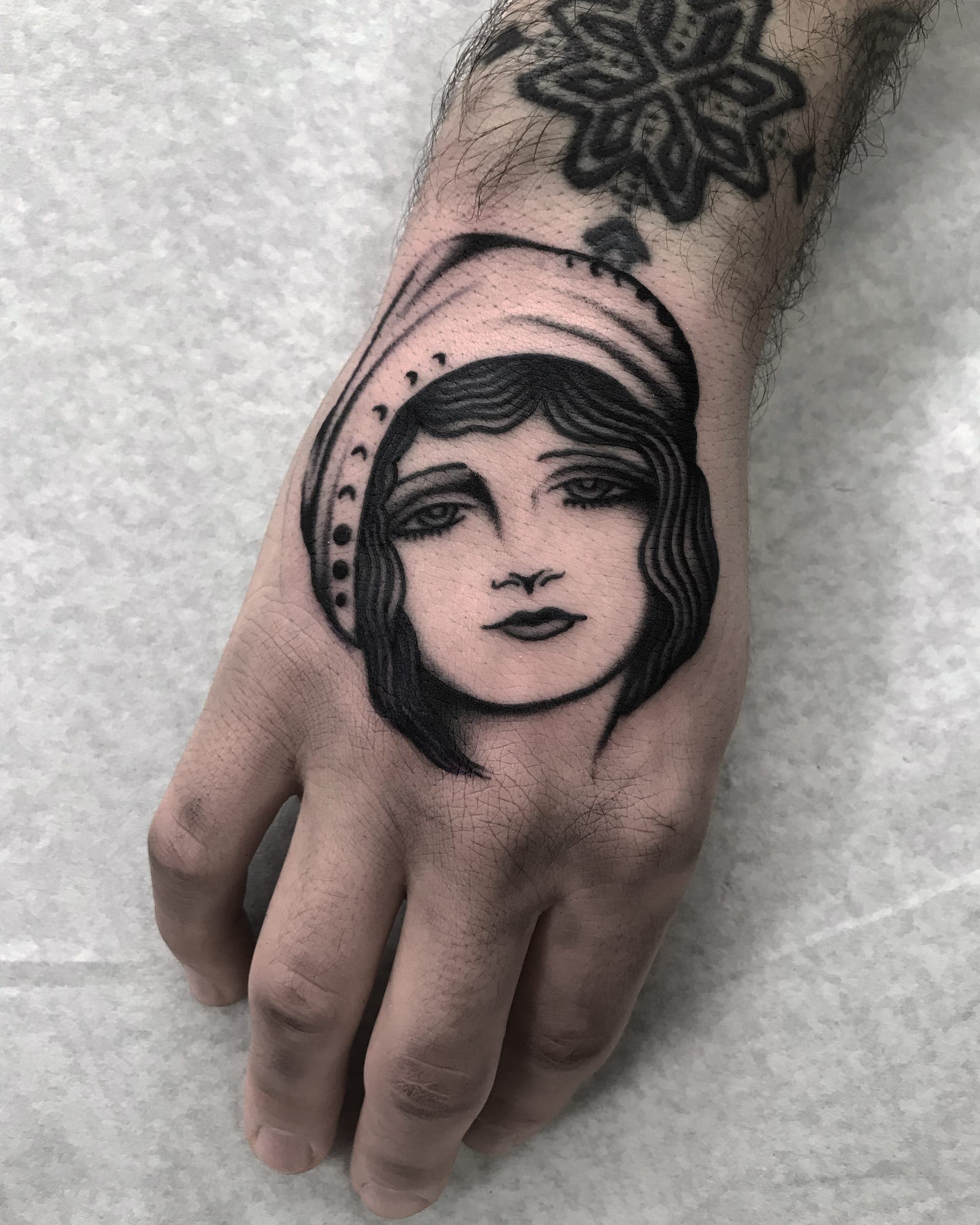 Traditional black ink lady head wearing a draped headscarf on the back of the hand