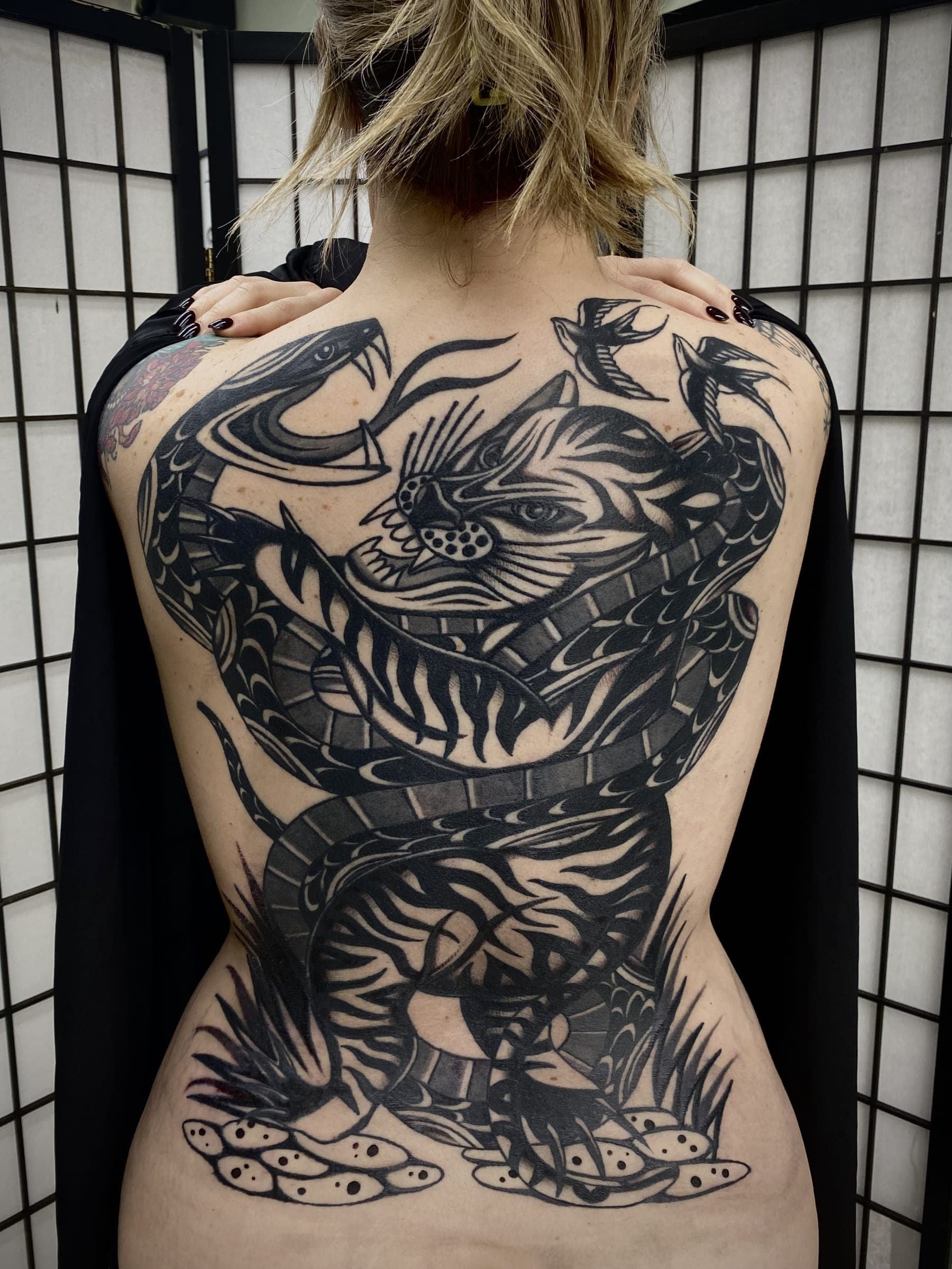 Large black tattoo of a striped tiger battling a coiled snake