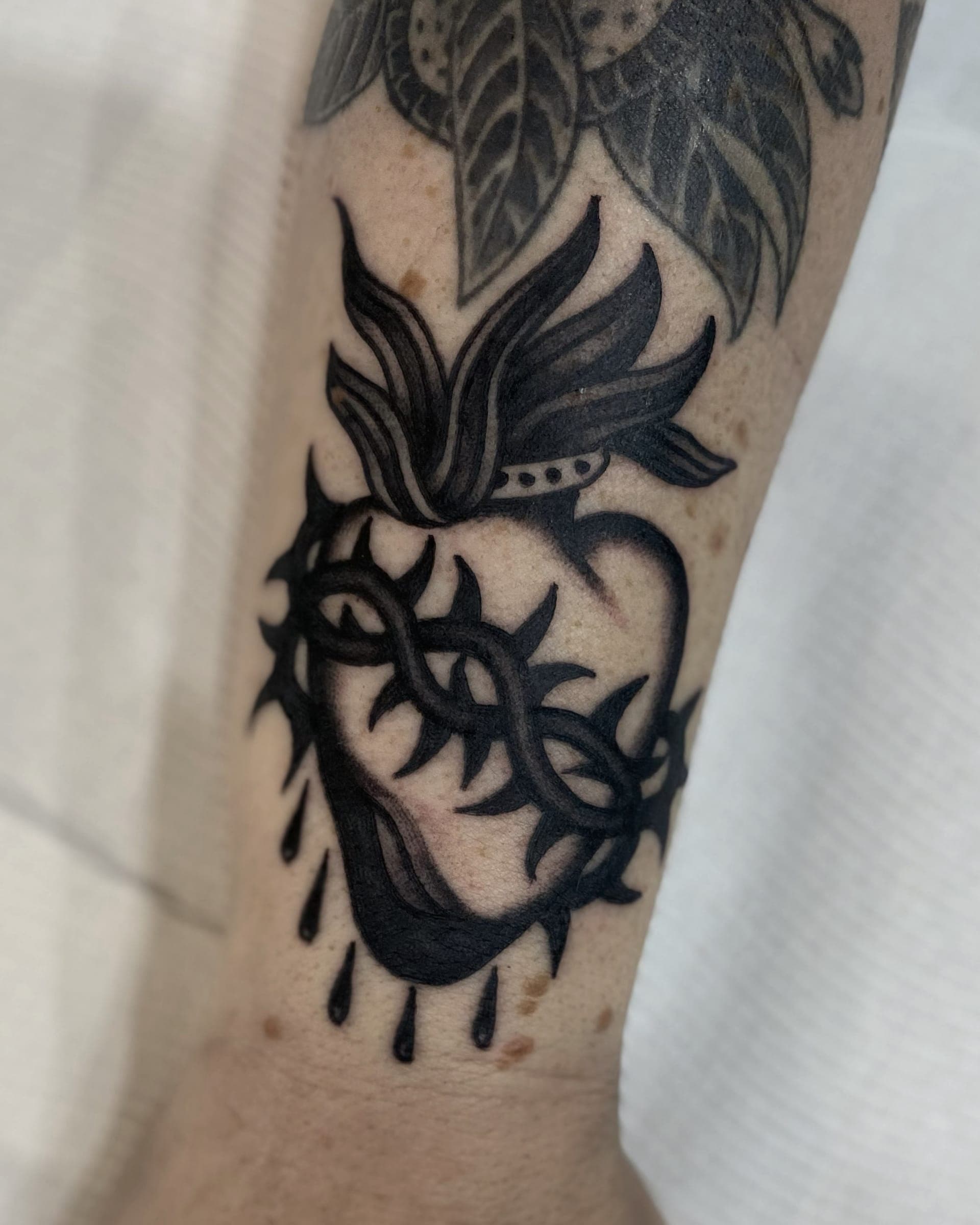 Black ink sacred heart wrapped in thorns with flame on top and blood drops below