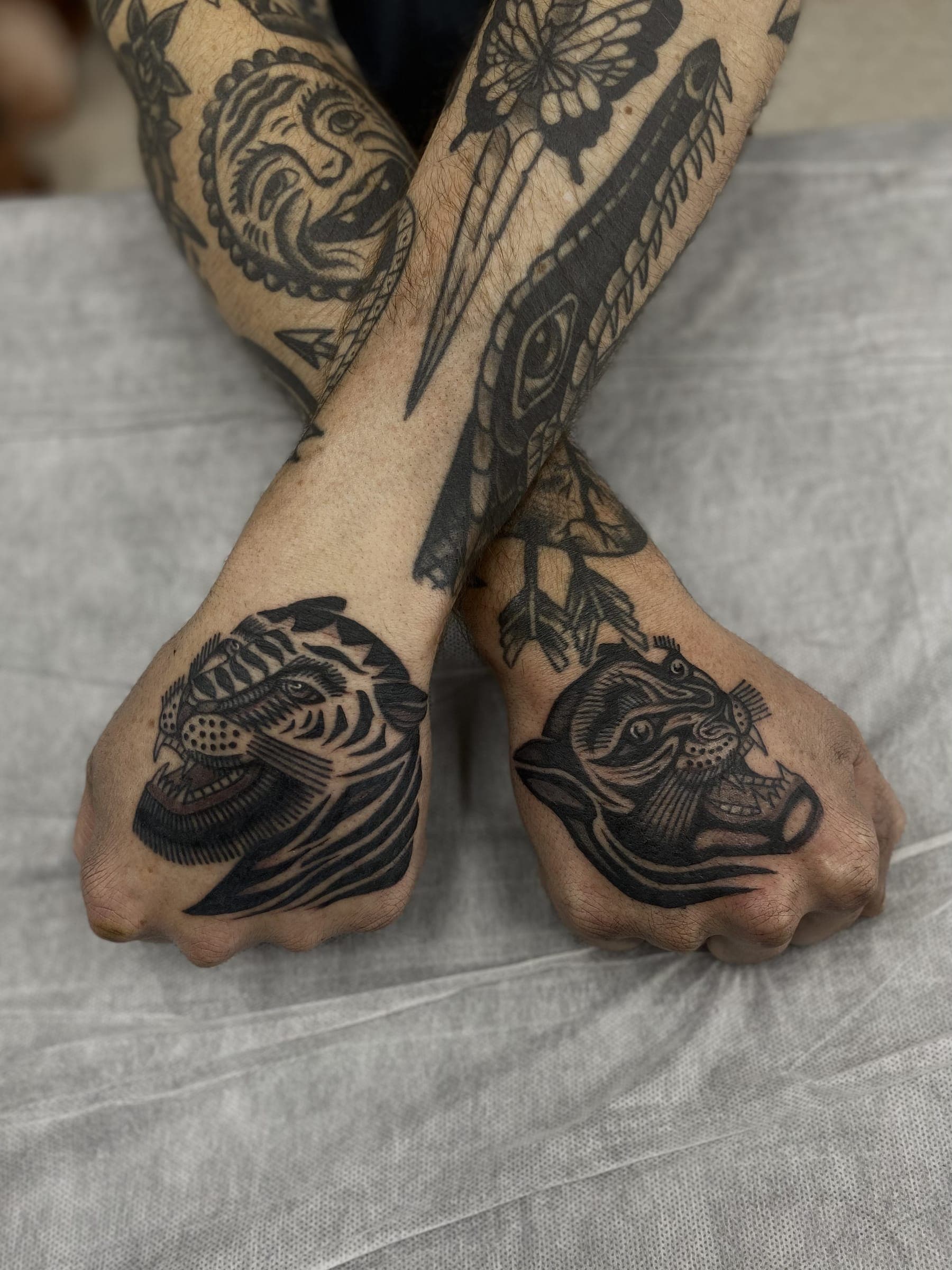 Snarling lion head tattooed on one and a tiger head on the other, both in traditional black