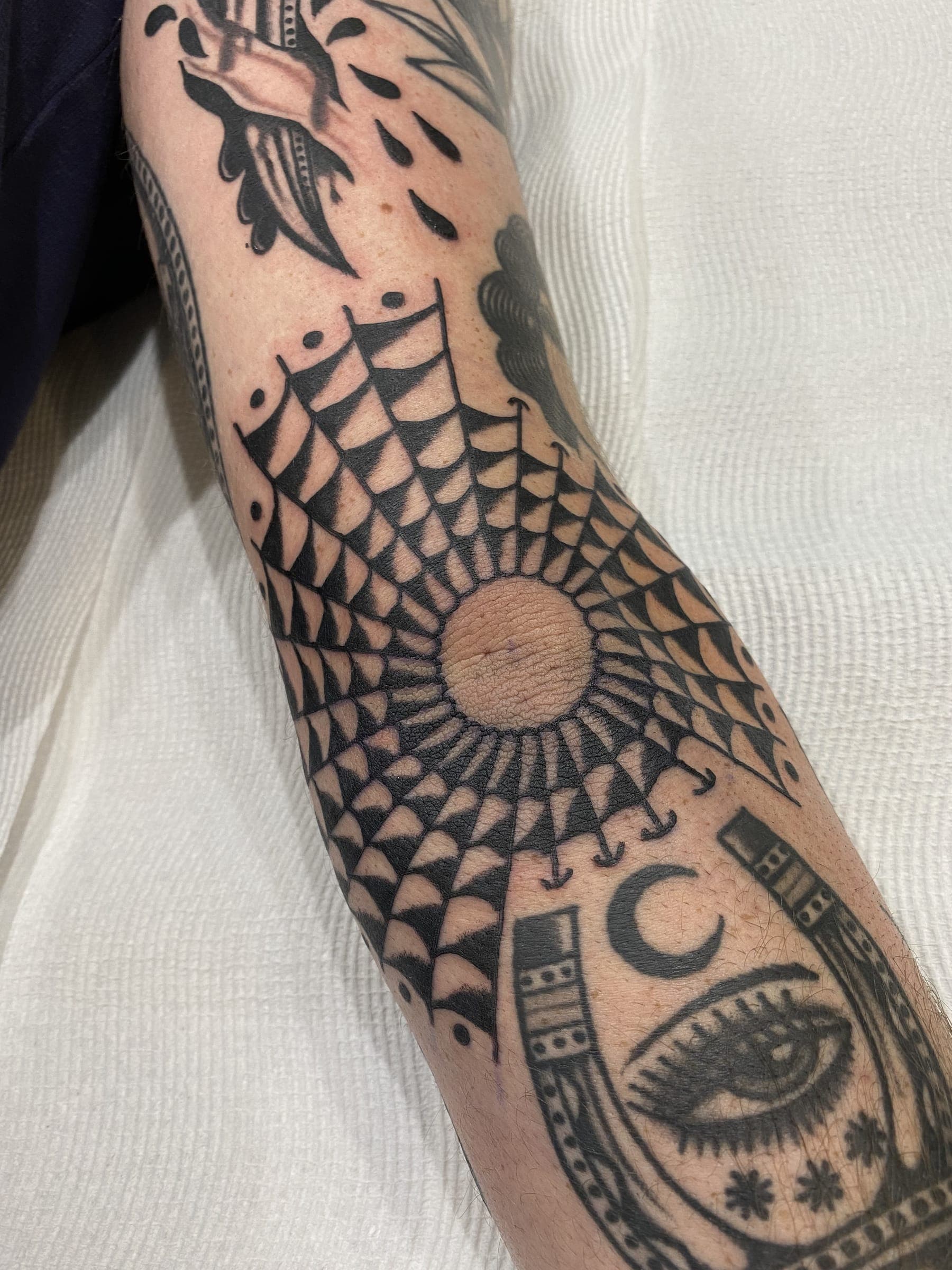 Radial sun mandala tattoo with concentric petal rings above a horseshoe and eye panel