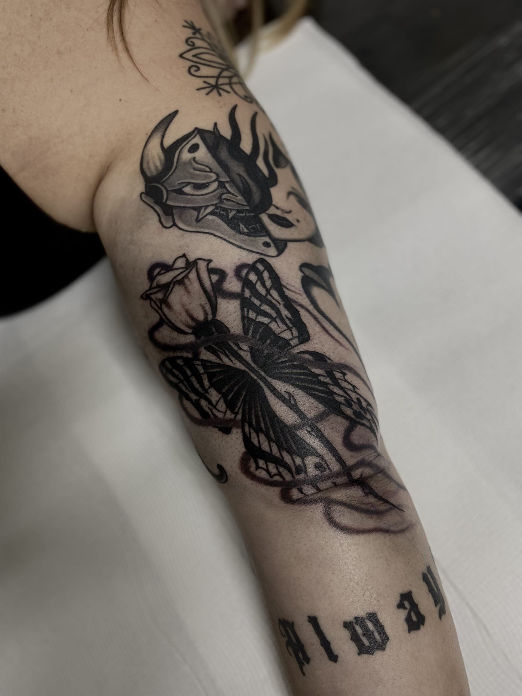 Black horned skull tattoo above a butterfly with patterned wings