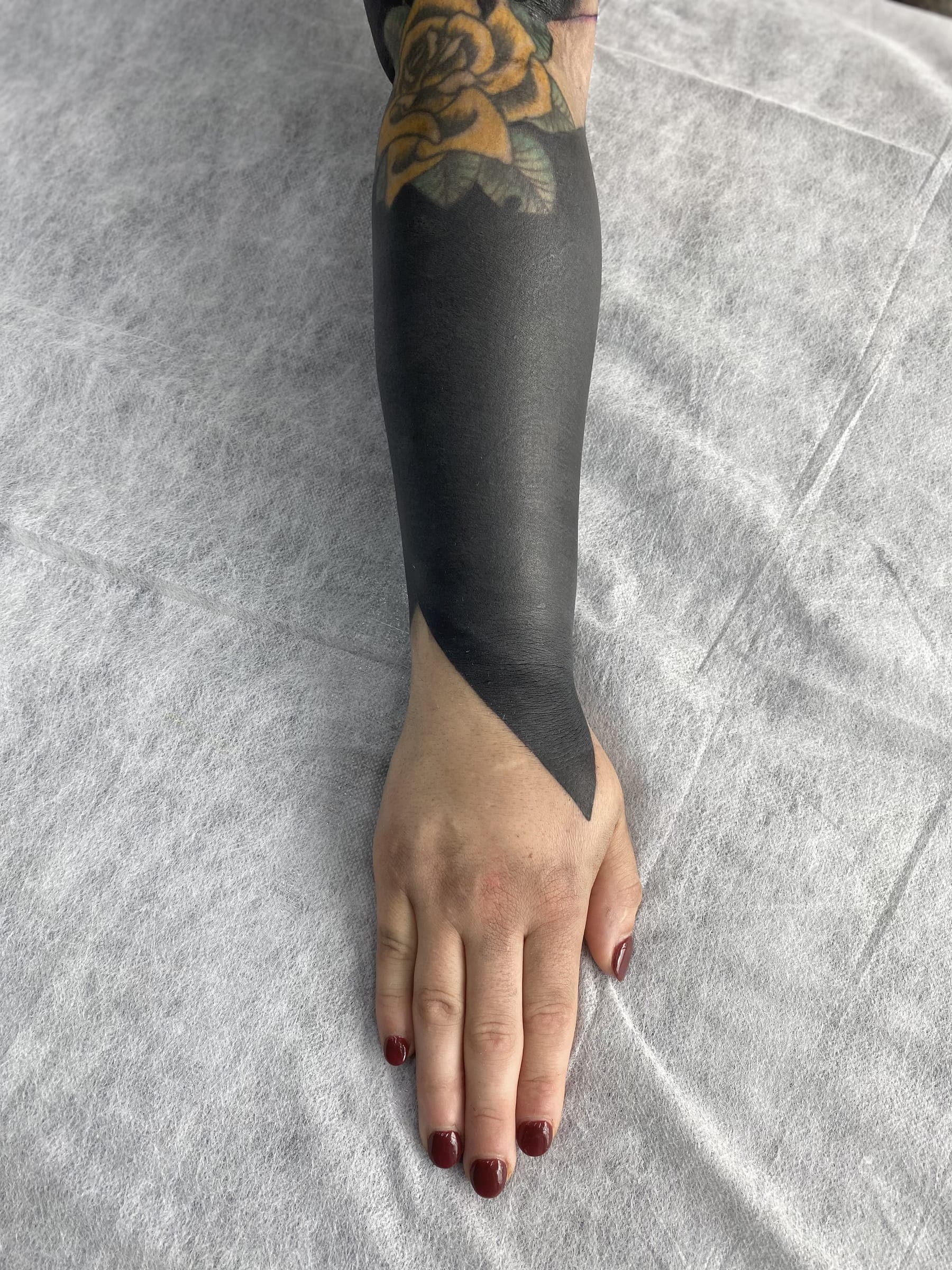 Solid black blackout tattoo finishing in a sharp V