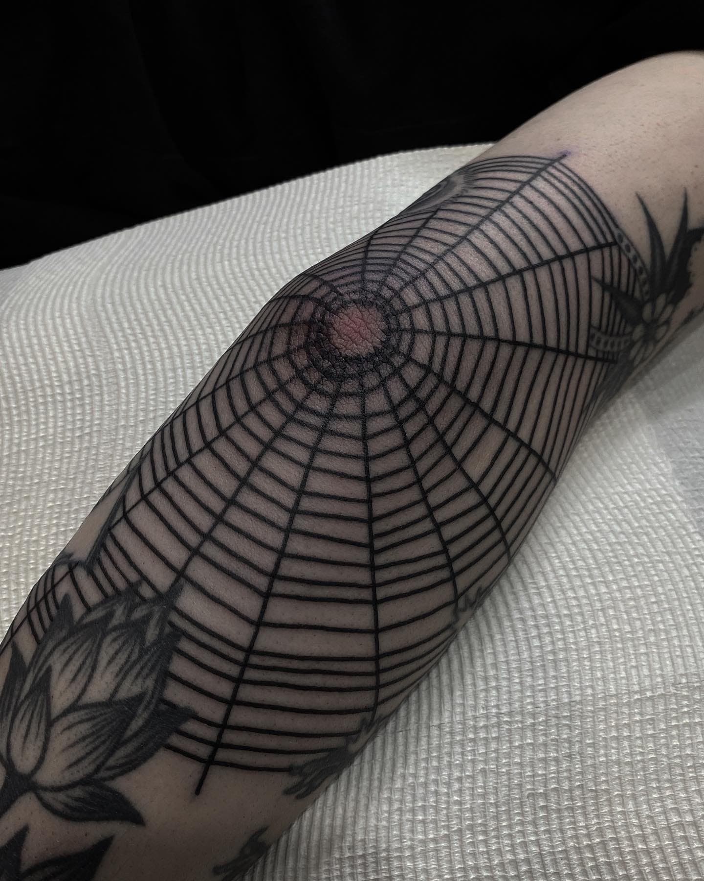 Black ink spider web tattoo radiating joint with red spider