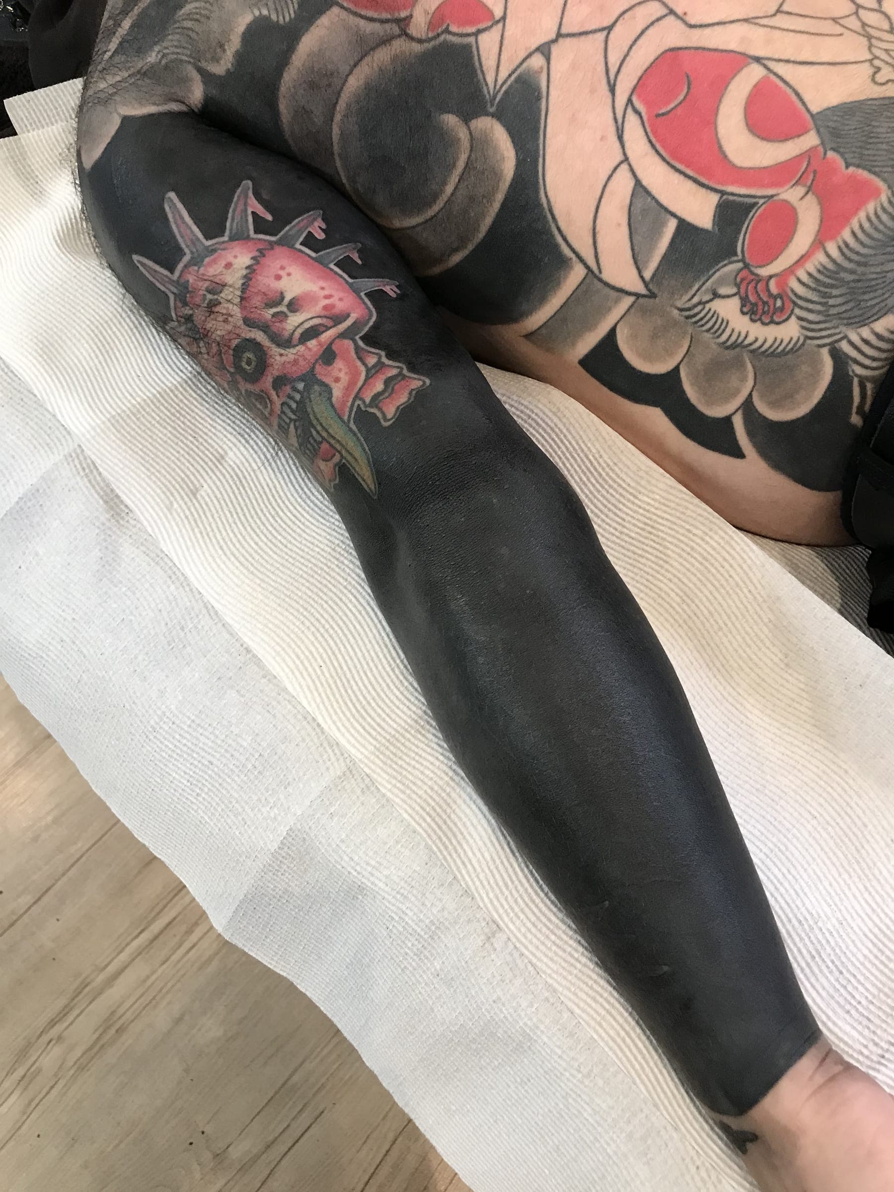 Red oni mask tattoo at the top of above a solid black fill running down