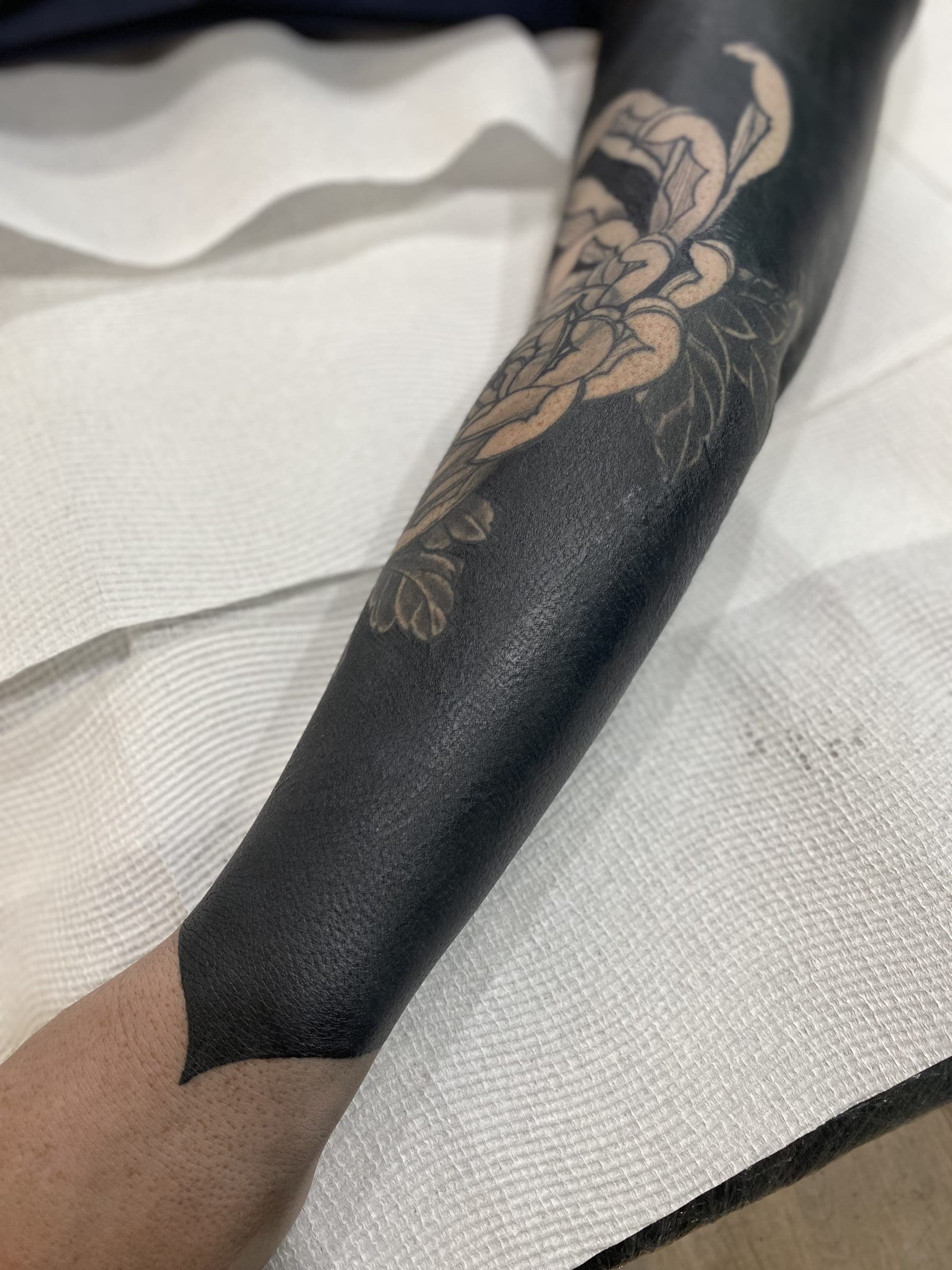 Solid black tattoo with a peony flower left in lighter negative space at crease