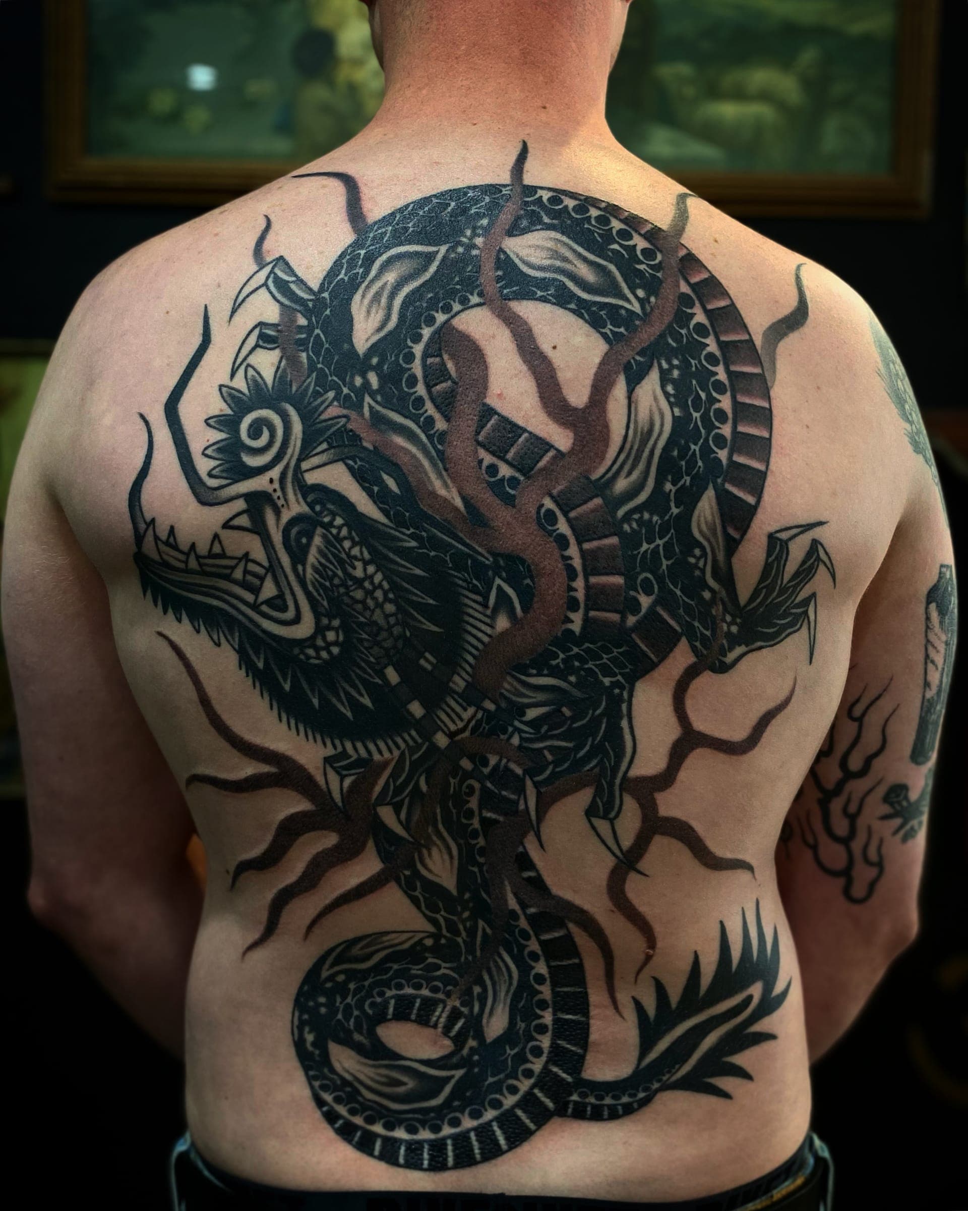Large black ink coiled dragon with horns and clawed limbs wrapping the full back