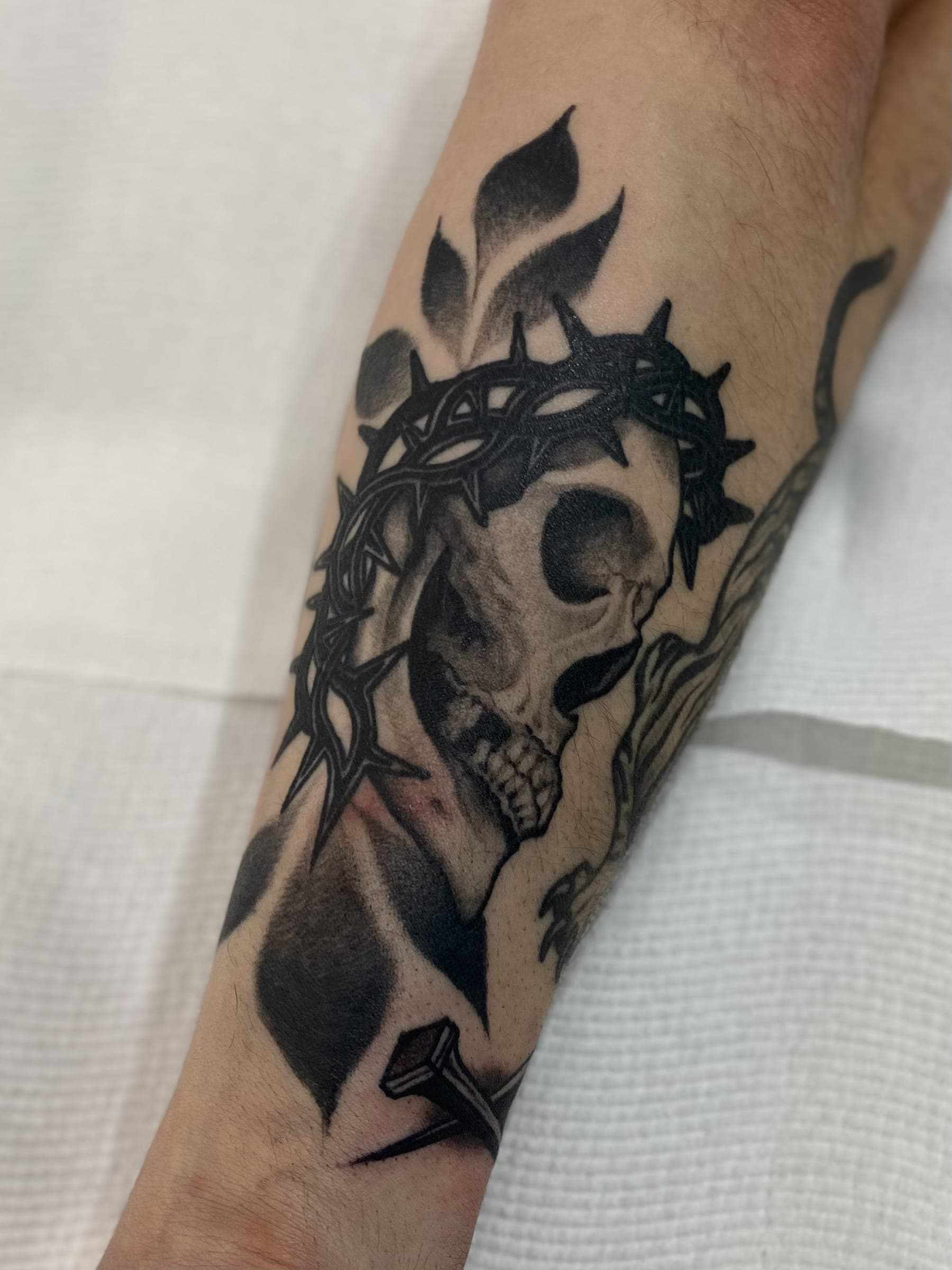 Traditional black and grey skull tattoo crowned with a thorny ring and pierced by a nail