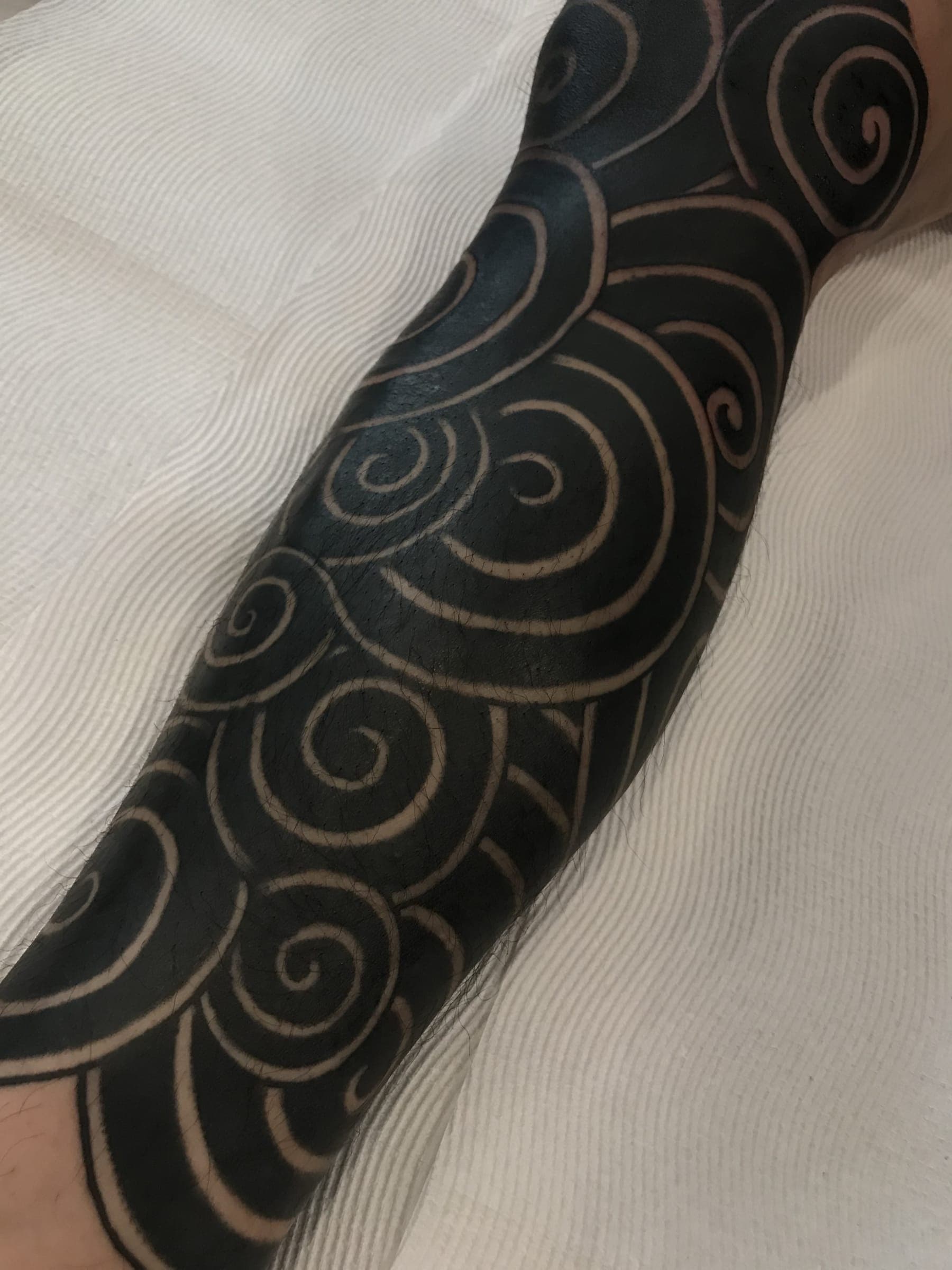Solid black tattoo with curling koru-style swirls left as negative space skin lines