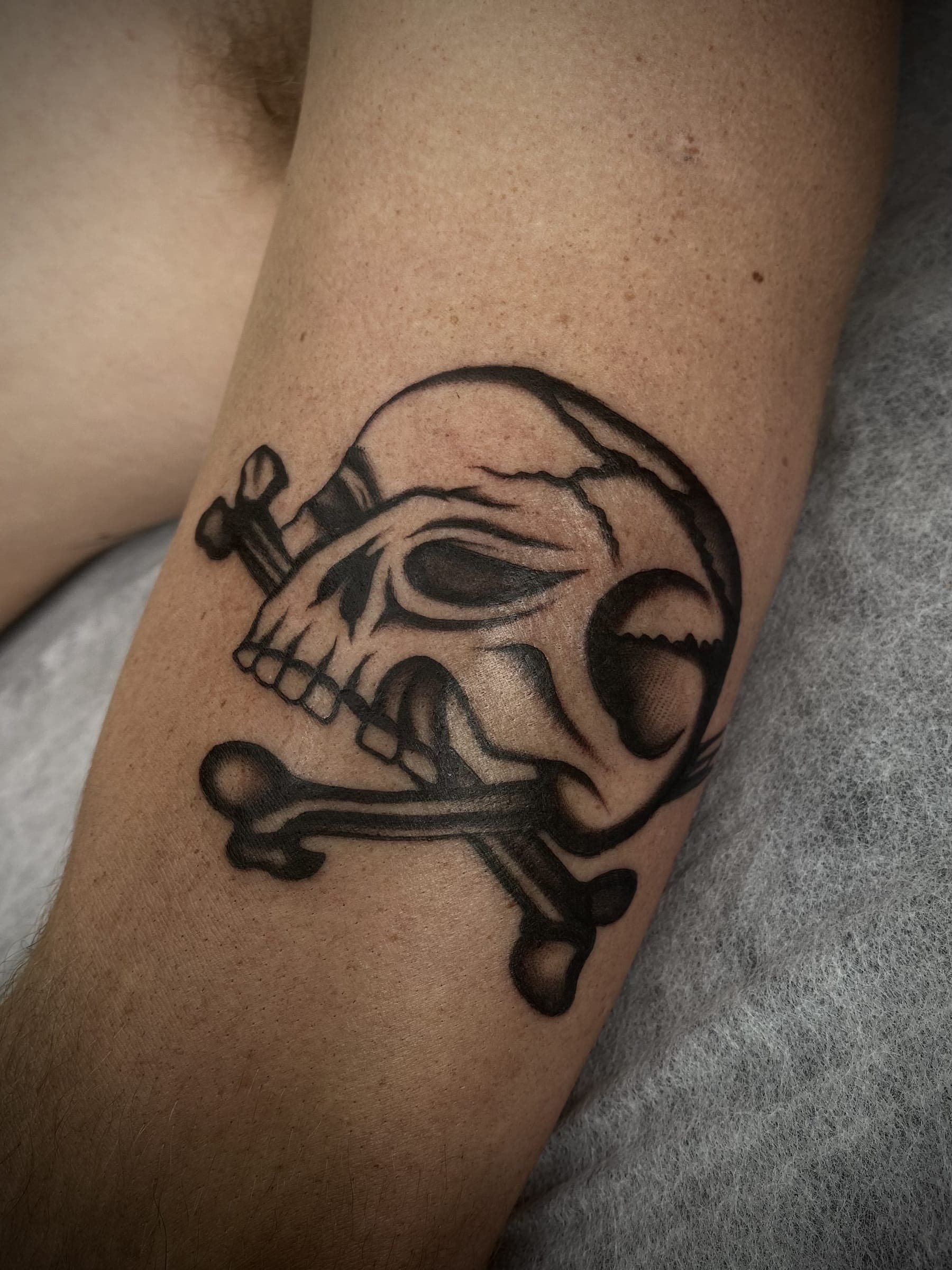 Black traditional skull and crossbones tattoo with cracked cranium