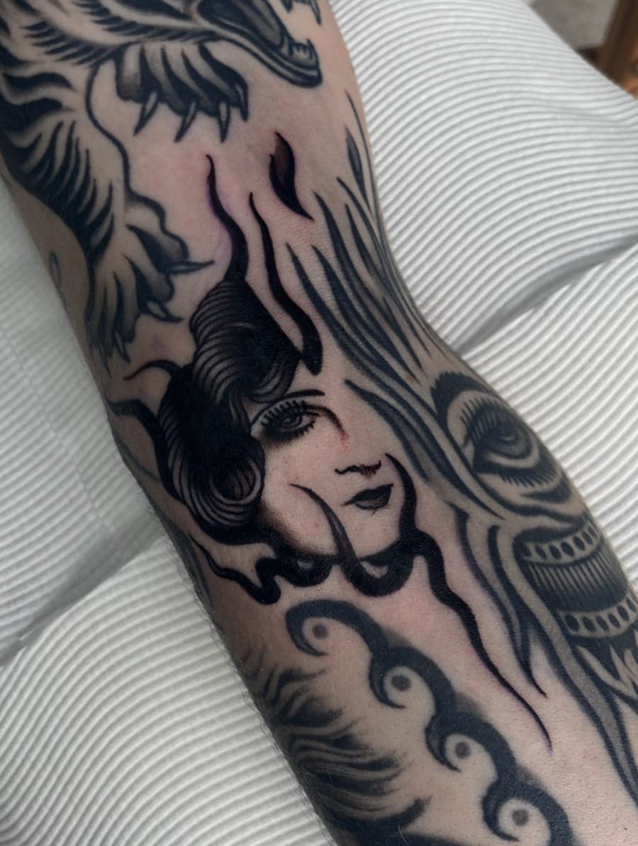 Black traditional lady head tattoo with flowing hair and flames inside a full coverage piece