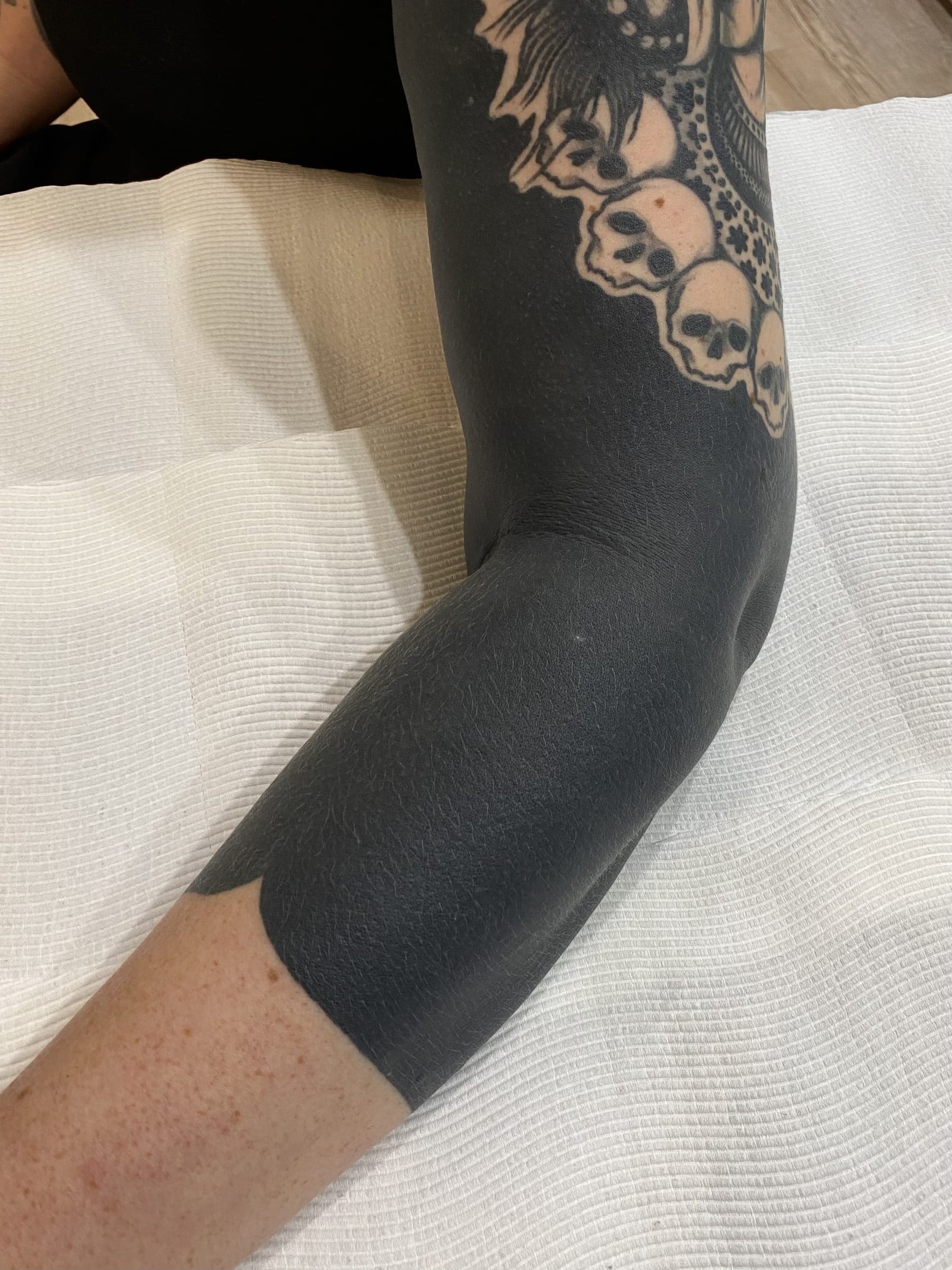 Solid black blackwork tattoo with a row of negative-space skulls