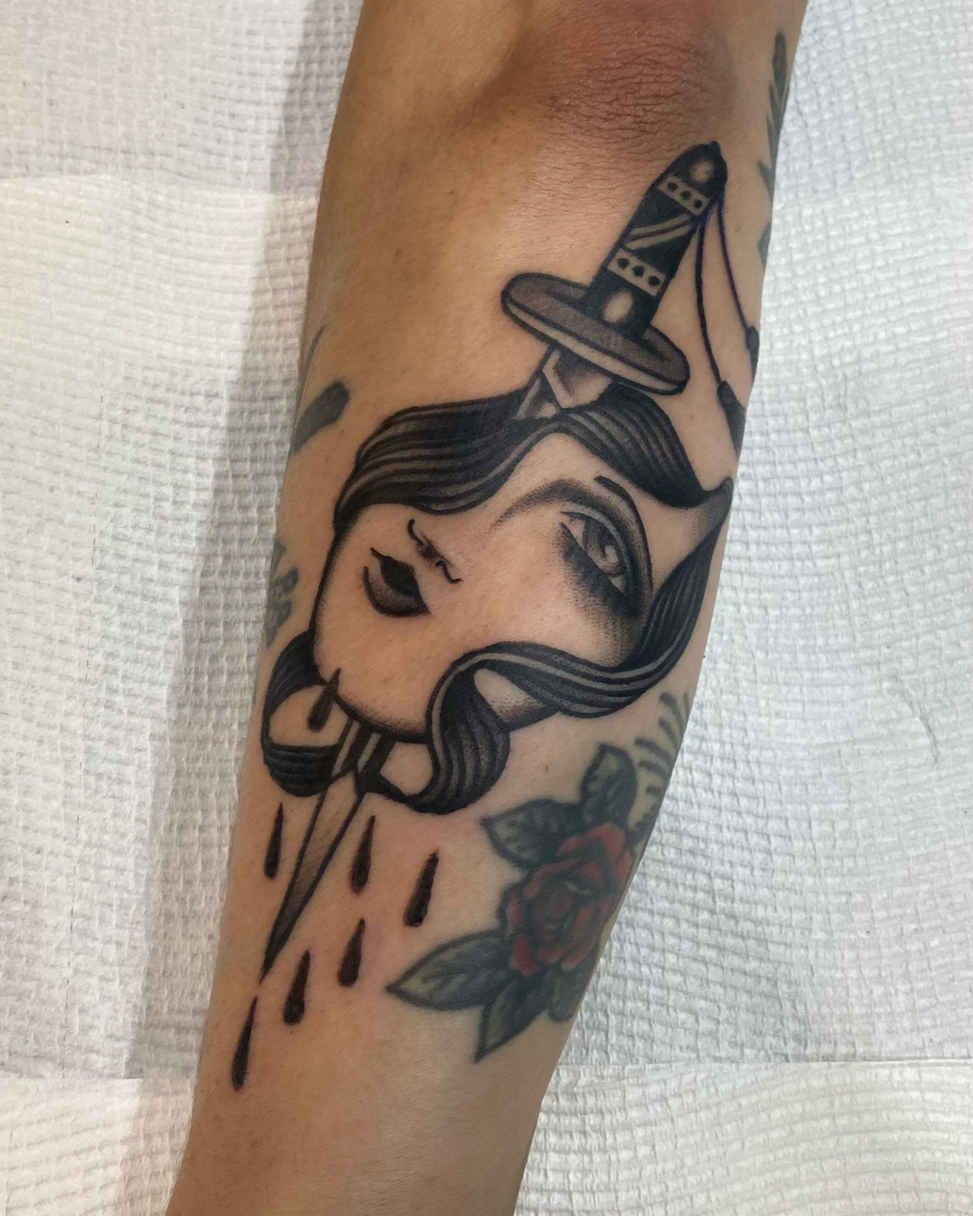 Dagger driven through a girl head with a weeping eye and red rose on the inner