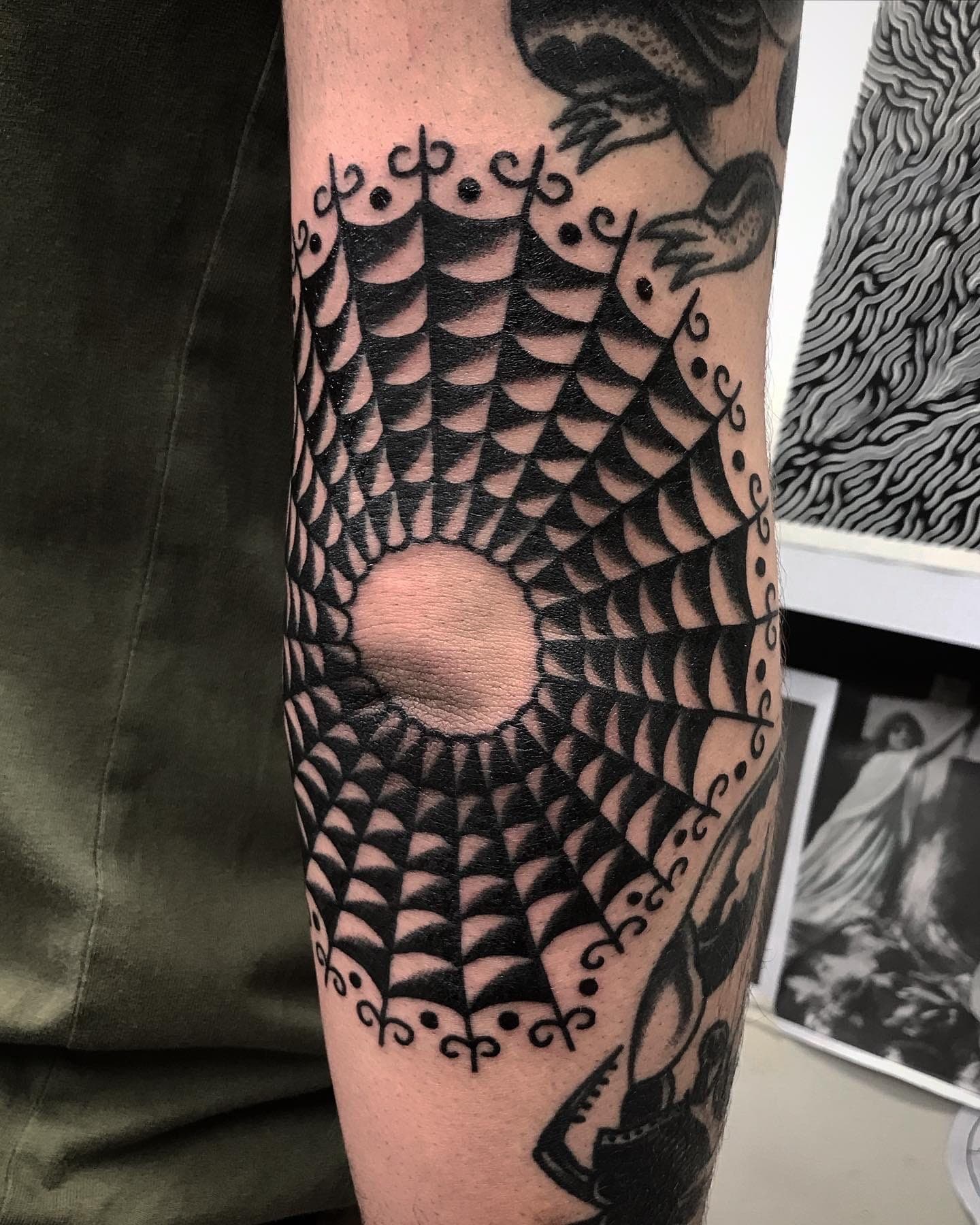 Traditional shaded spiderweb with a negative-space centre and scrollwork border across the forearm