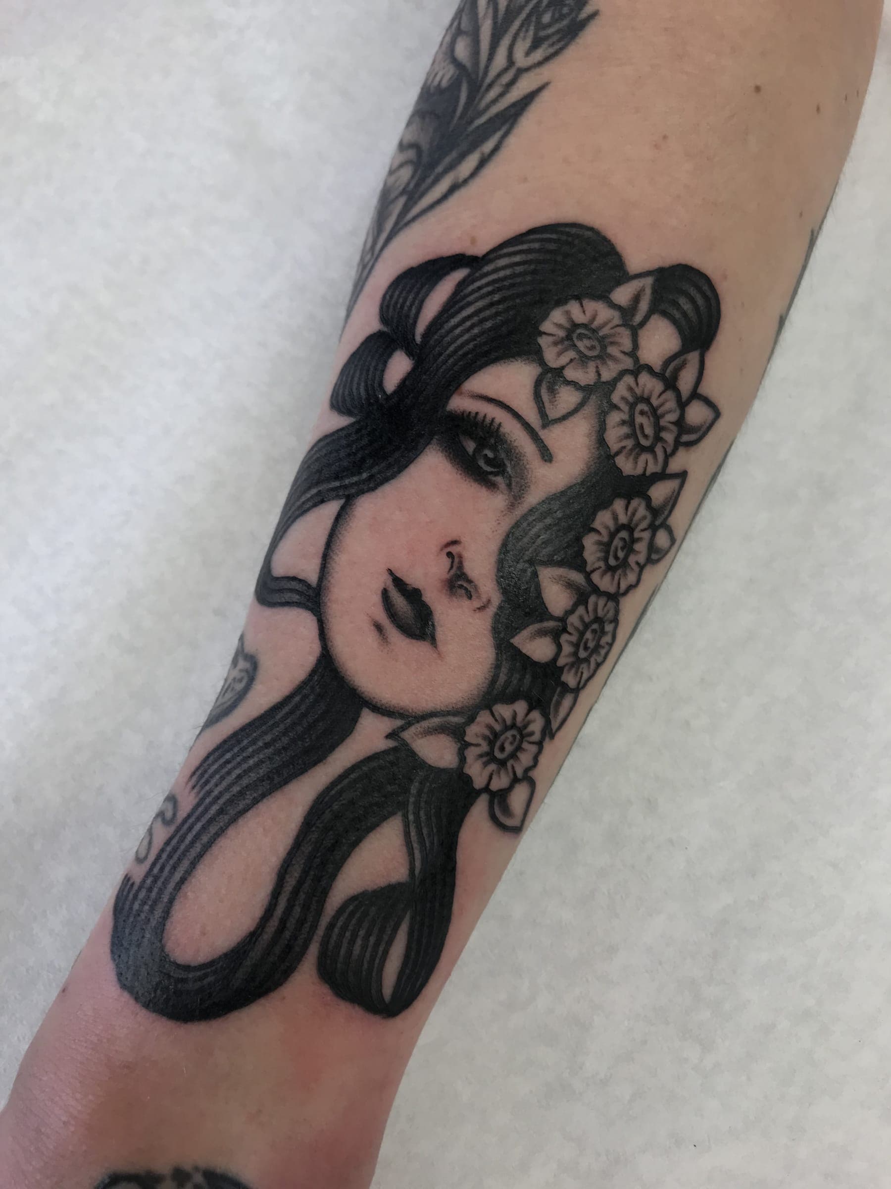 Black and grey neo-traditional lady head with long flowing hair and daffodils on the forearm
