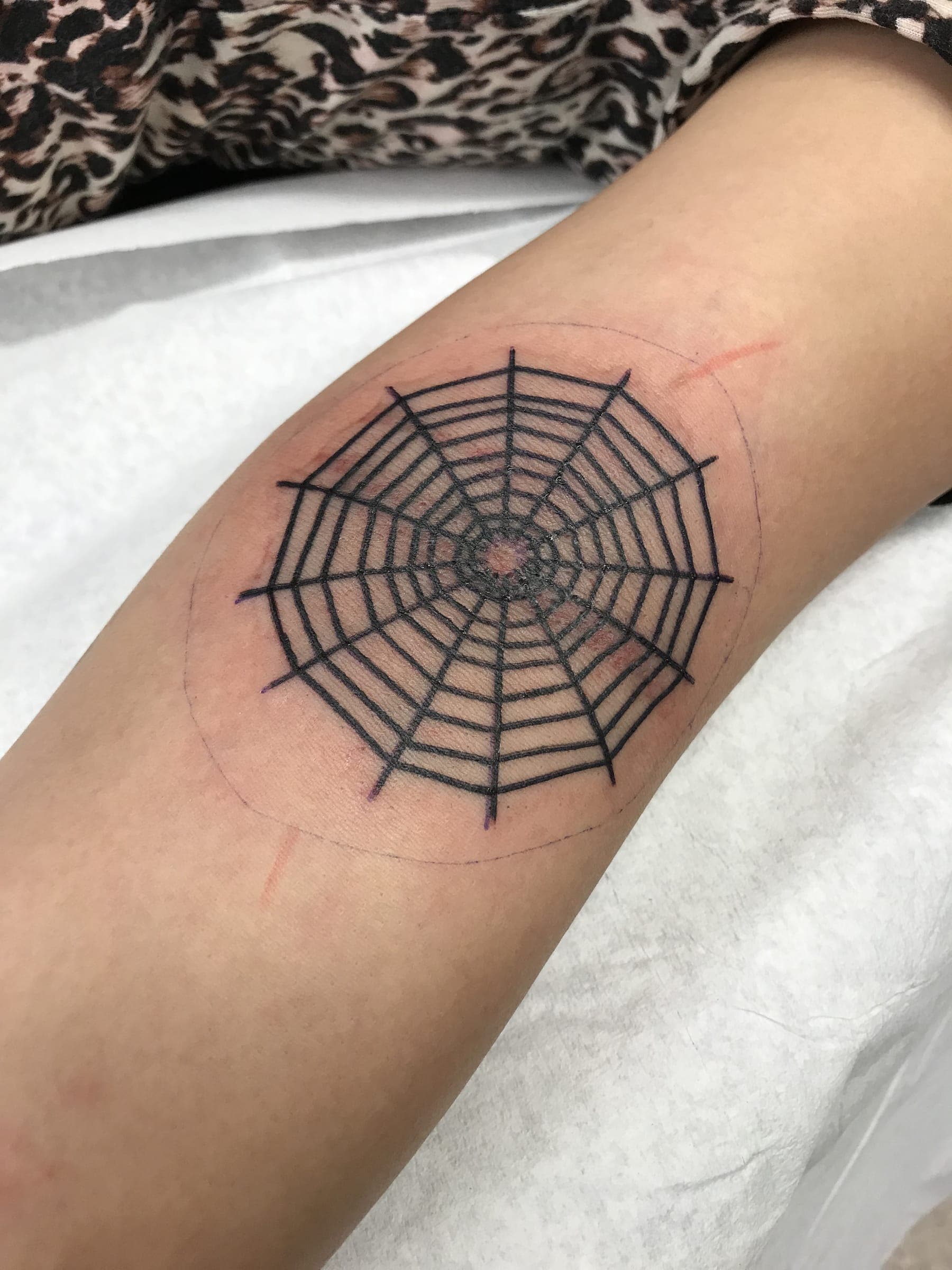 Fine line single-needle spiderweb with a small spider behind the knee